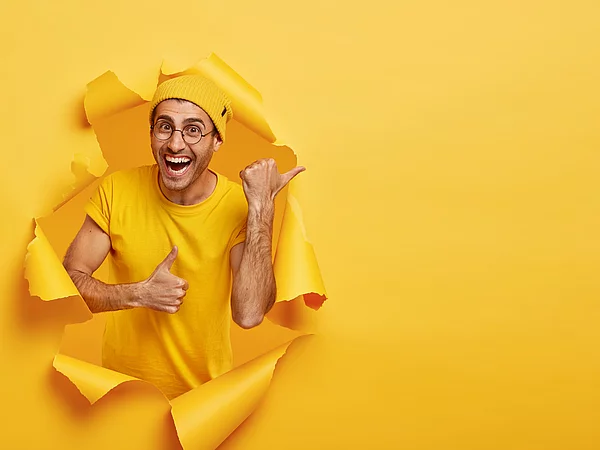 Mann lacht und schuat aus einer Papierrolle